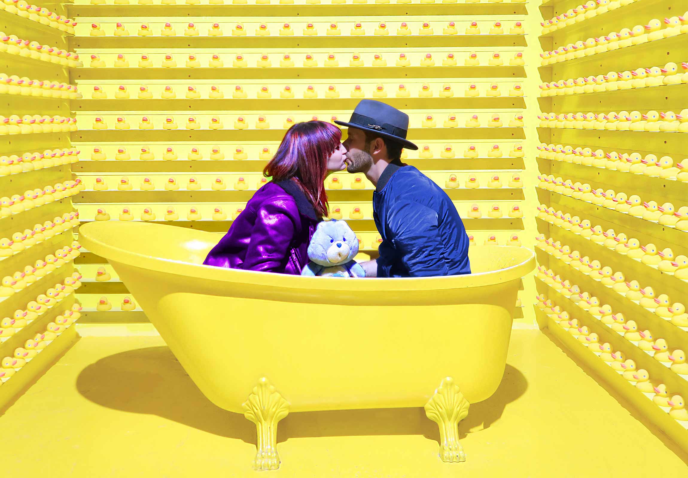 Two people in a yellow room, kissing in a bathtub